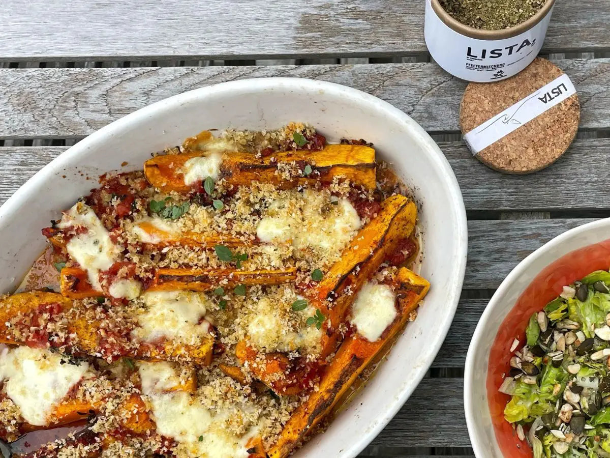 Butternut-Parmigiana in einer weißen Auflaufform mit Mozzarella und Panko-Kruste auf einem grauen Holztisch
